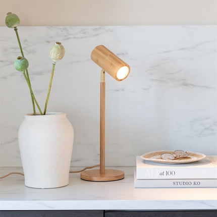 Lampe de table Java en bambou naturel allumée, diffusant une lumière chaude et dirigée depuis sa tête orientable