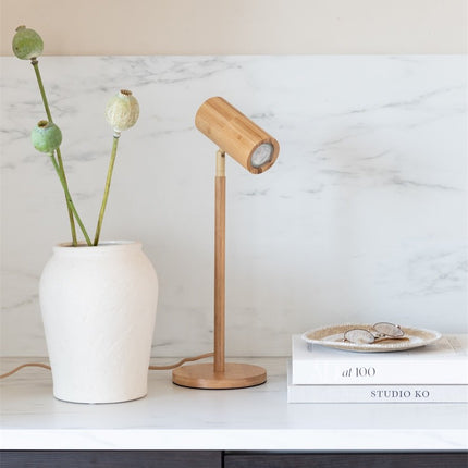 Lampe de table Java en bambou naturel avec tête orientable posée sur un meuble en marbre blanc, à côté d'un vase en céramique