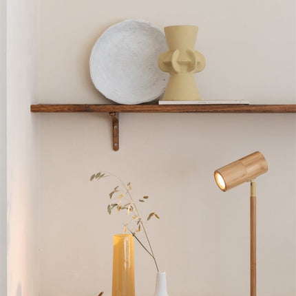Lampe de table Java en bambou naturel allumée devant un mur clair, avec vases décoratifs et branchages en arrière-plan