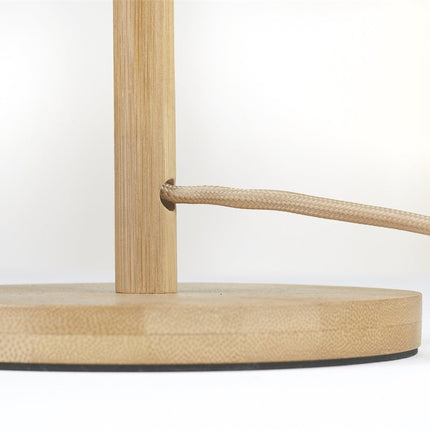 Gros plan sur le socle rond en bambou naturel de la lampe Java, avec passage du câble textile beige tressé