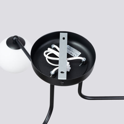 plafonnier 3 globes opale sur bras noir, vue sur fond coloré