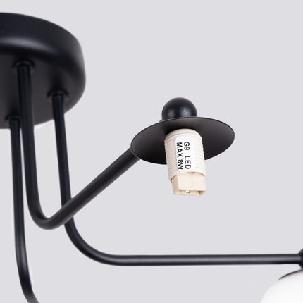 plafonnier 5 globes opale sur bras noir, vue sur fond coloré