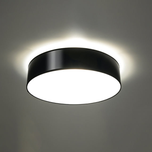 Plafonnier Arène 55 noir allumé au plafond, lumière douce diffusée par le diffuseur opale