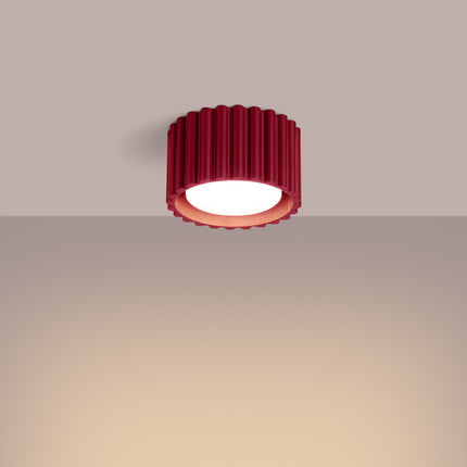 Plafonnier Aura bordeaux allumé au plafond, halo de lumière chaude sur mur beige
