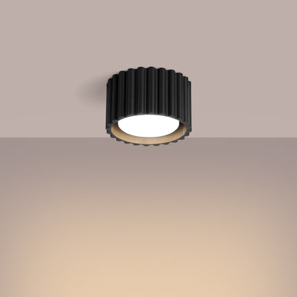 Plafonnier Aura noir cannelé allumé diffusant une lumière chaude au plafond