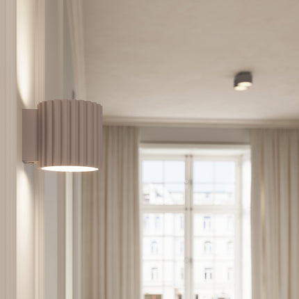 Plafonnier Aura taupe allumé dans un intérieur clair près d'une fenêtre