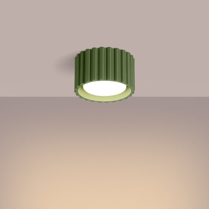 Plafonnier Aura vert olive diffusant une lumière chaude sous un plafond aux tons rosés