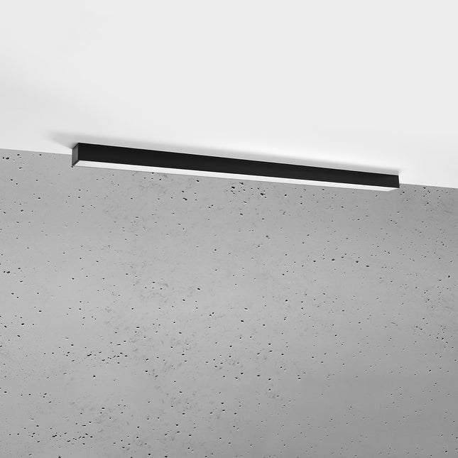 Plafonnier barre moderne LED noir 118 cm installé au plafond au-dessus d'un mur de béton