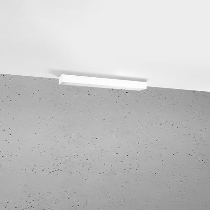 Plafonnier barre moderne LED blanc installé au plafond au-dessus d'un mur de béton