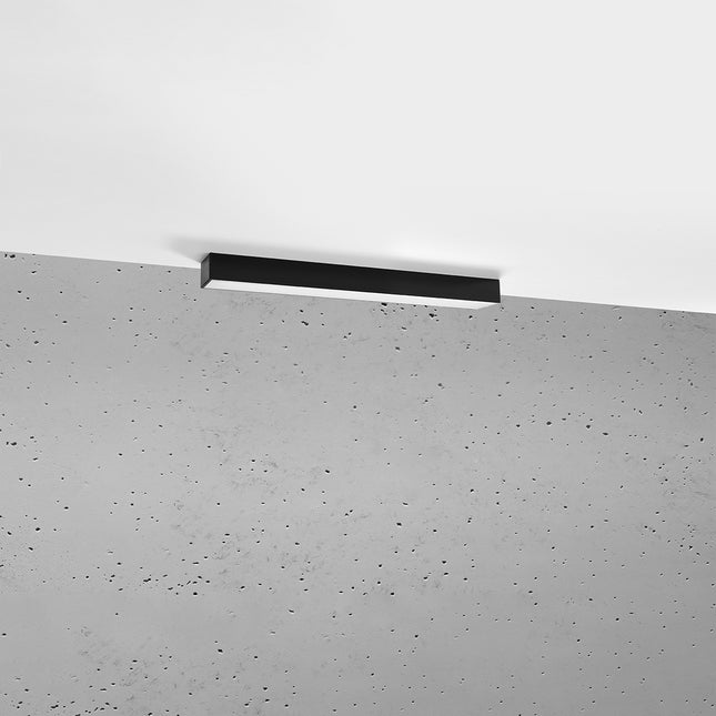 Plafonnier barre moderne LED noir installé au plafond au-dessus d'un mur de béton