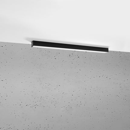 Plafonnier barre moderne LED noir 90 cm installé au plafond au-dessus d'un mur de béton