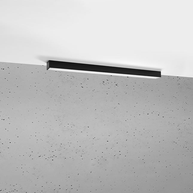 Plafonnier barre moderne LED noir 90 cm installé au plafond au-dessus d'un mur de béton