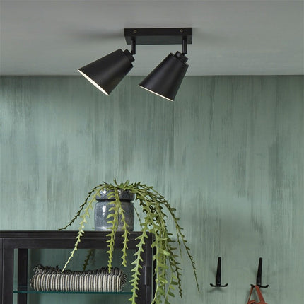 Vue large du plafonnier Bremen à deux spots noirs installé dans un salon aux tons verts