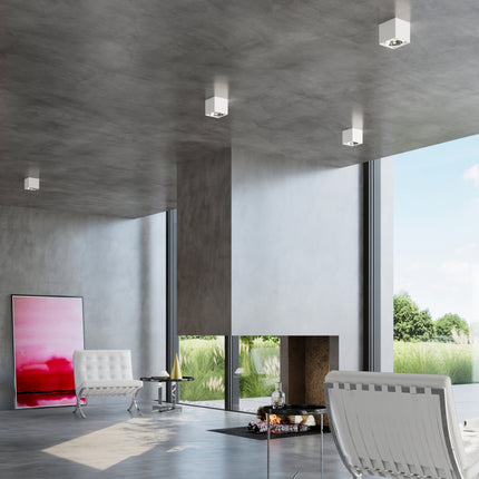 Plafonniers carrés blancs au plafond béton d'un séjour design avec fauteuils blancs