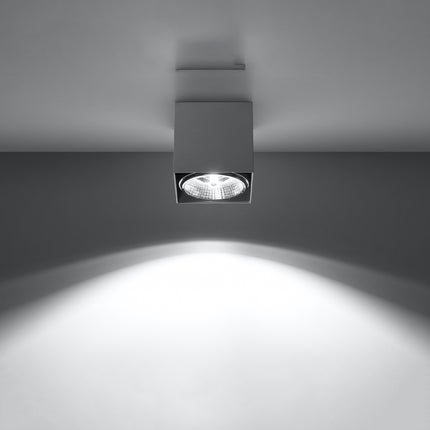 Plafonnier carré gris allumé projetant un faisceau lumineux net vers le sol sur fond clair