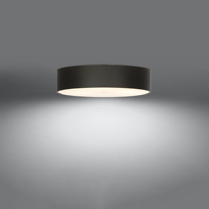 Plafonnier Cercle Plein noir 50 cm vu de trois quarts, large tambour en tissu et diffuseur en verre éclairé.