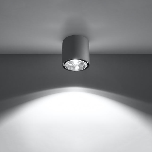 Plafonnier circulaire gris allumé projetant un faisceau lumineux net sur le mur et le sol
