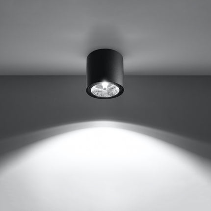 Plafonnier circulaire noir allumé projetant un faisceau lumineux net sur le mur et le sol