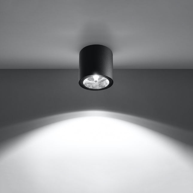 Plafonnier circulaire noir allumé projetant un faisceau lumineux net sur le mur et le sol