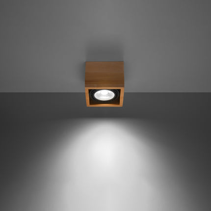 Plafonnier spot cube bois naturel projetant un faisceau lumineux sur un mur gris
