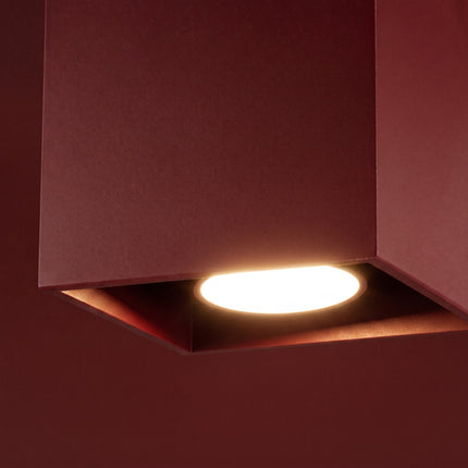 Plafonnier Cube LED bordeaux sur fond coloré, vue de trois quarts