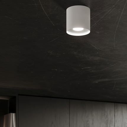Plafonnier blanc allumé au plafond d'une pièce sombre, effet lumineux discret
