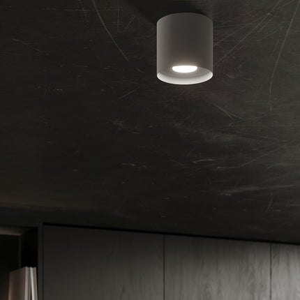 Plafonnier gris allumé au plafond d'une pièce sombre, effet lumineux discret