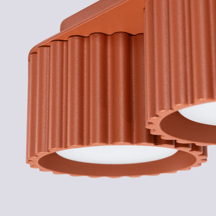 Détail des rainures verticales et des diffuseurs du plafonnier Aura rouge ocre en aluminium