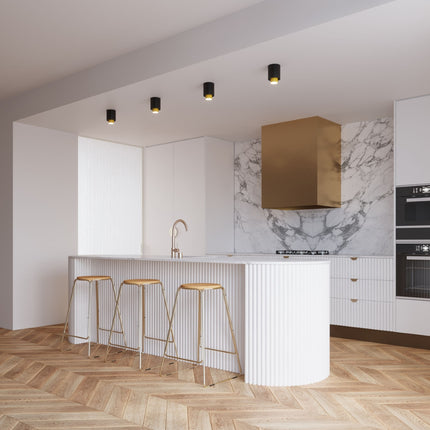 Quatre plafonniers double cylindre noir et laiton alignés au plafond d'une cuisine moderne avec îlot marbre