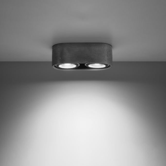 Plafonnier double spot en béton brut allumé, faisceaux lumineux dirigés vers le bas