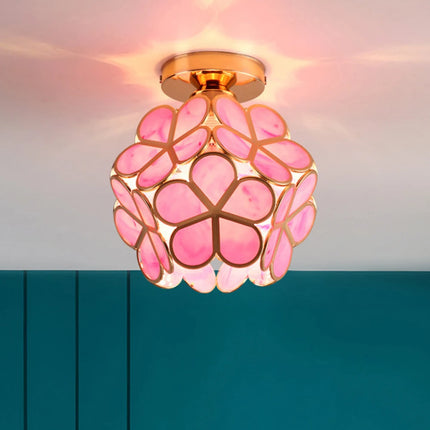 Plafonnier fleur en verre à pétales rose présenté devant un mur bleu canard