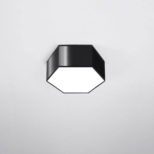 Plafón Hexagonal Pure 13 negro encendido sobre fondo gris oscuro, luz cálida difundida por el ojo de buey blanco.