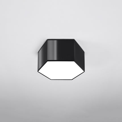 Plafonnier Hexagonal Pure 15 noir allumé sur fond gris foncé, lumière chaude diffusée par le hublot blanc.
