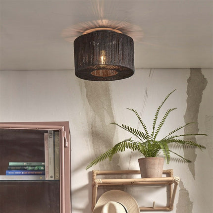 Iguazu ceiling light in braided black jute hanging on the ceiling of a living room, bohemian atmosphere with plant and shelf in rattan