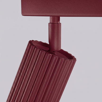 Plafonnier Oslo barre 6 spots orientables 117 cm bordeaux sur fond coloré, vue de trois quarts