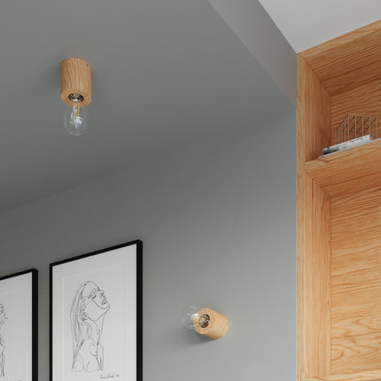 Deux luminaires cylindre en bois montés au plafond et au mur gris, ampoules filament apparentes.