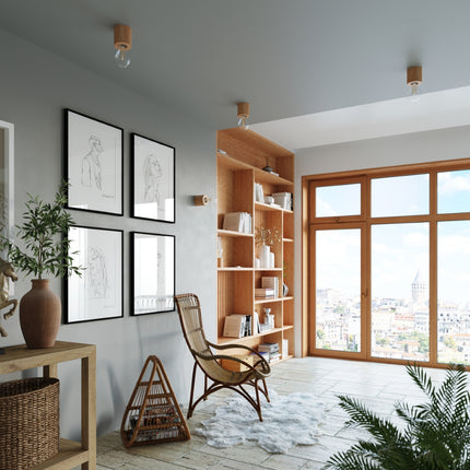 Séjour scandinave lumineux avec des luminaires cylindre en bois au plafond, cadres et fauteuil en rotin.