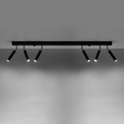Carril de 6 focos de acero negro encendido proyectando sus haces sobre una pared clara