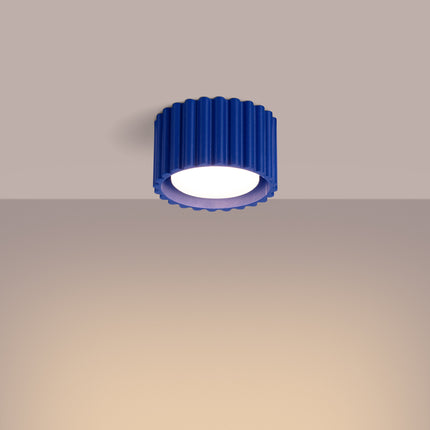 Plafonnier spot Aura bleu outremer allumé projetant une lumière chaude sur un mur beige