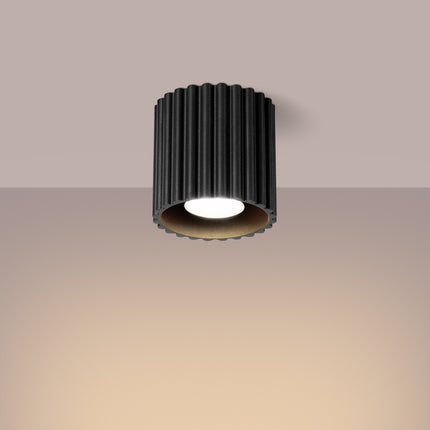 Plafonnier spot Aura noir allumé au plafond diffusant une lumière chaude dans un intérieur