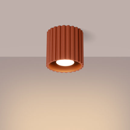 Plafonnier Aura rouge terracotta allumé au plafond, halo chaud diffusé vers le sol