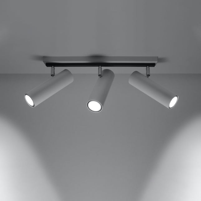 Plafonnier tube ajustable blanc à trois spots allumé, faisceaux dirigés sur un mur gris