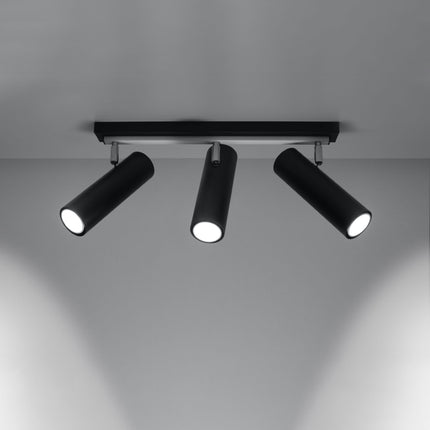 Plafonnier tube ajustable noir à trois spots allumé, faisceaux dirigés sur un mur gris
