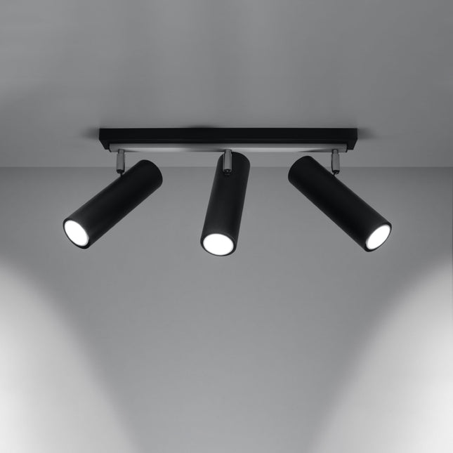 Plafonnier tube ajustable noir à trois spots allumé, faisceaux dirigés sur un mur gris