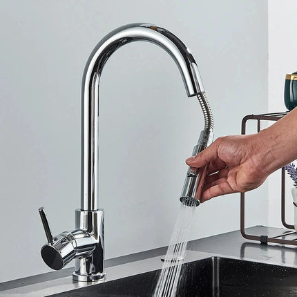 Mano que tira de la ducha retráctil de un grifo mezclador de cocina cromado