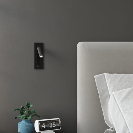 Spot liseuse noir au-dessus d'un chevet, ambiance feutrée de chambre contemporaine