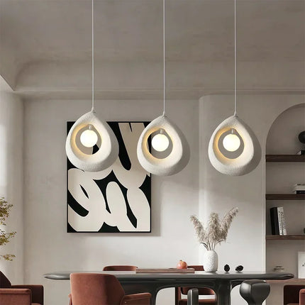 Trois suspensions anneau sablé blanc au-dessus d'une table à manger, diffusant une lumière chaude dans un intérieur épuré