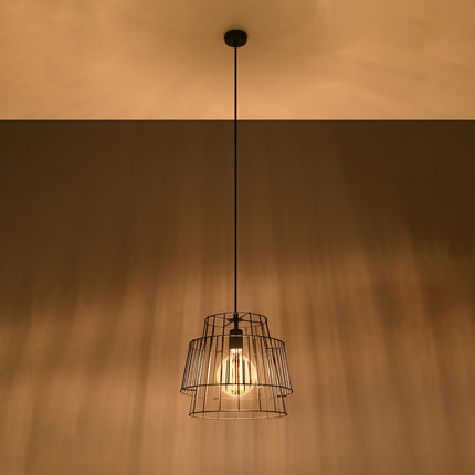 Suspension cage noire allumée diffusant une lumière chaude et un jeu d'ombres graphiques sur le plafond.
