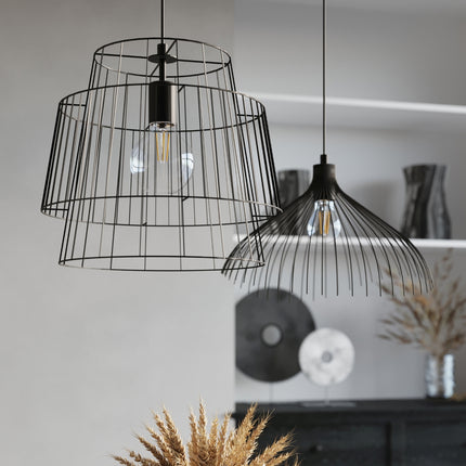 Gros plan de la suspension cage noire à double cage ajourée et ampoule à filament, dans un intérieur clair.