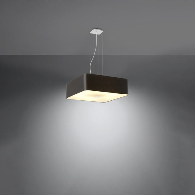 Suspension carrée noire allumée diffusant une lumière chaude et douce sur un mur gris